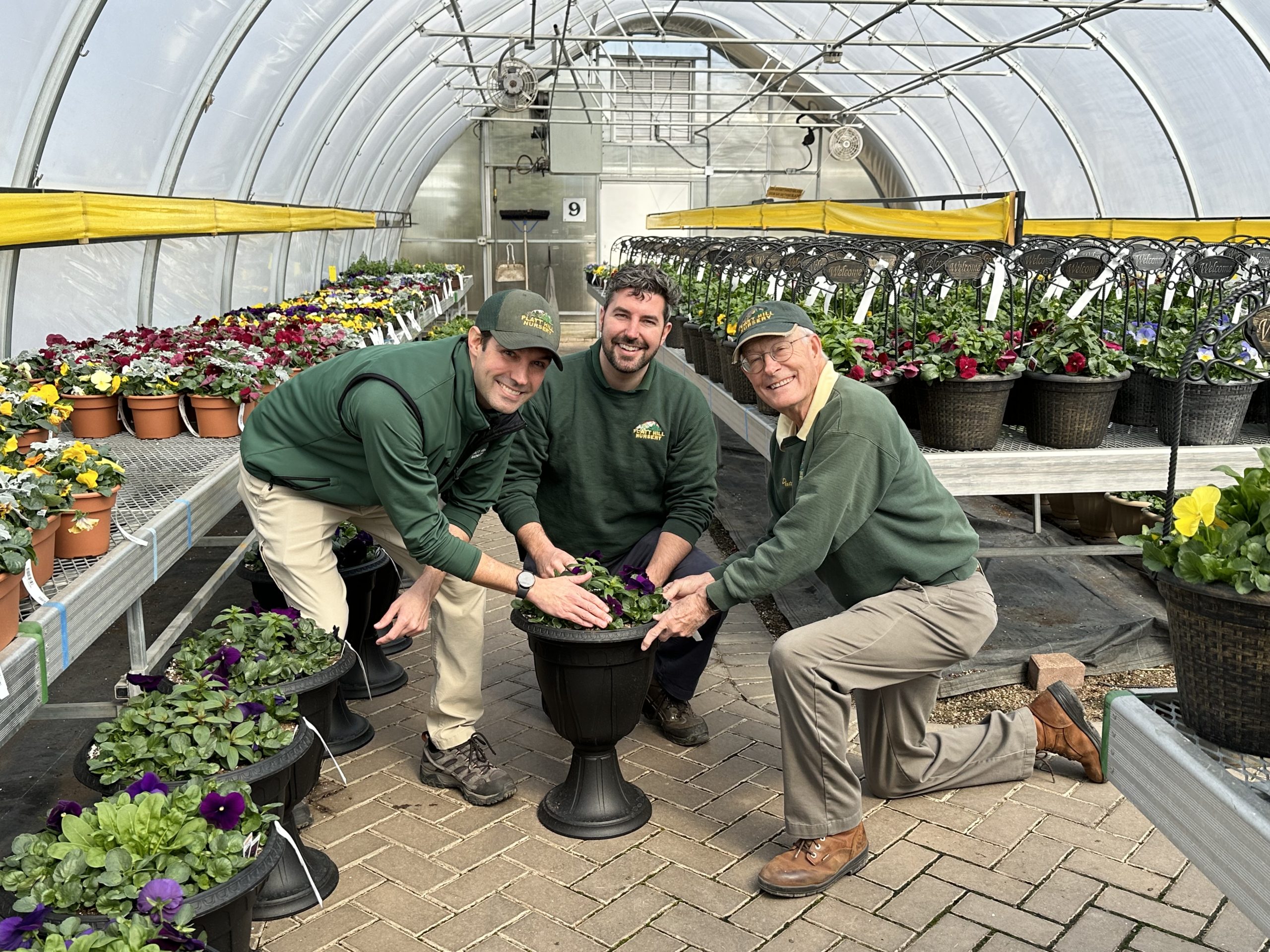 a group of men in green shirts and hats in a greenhouse